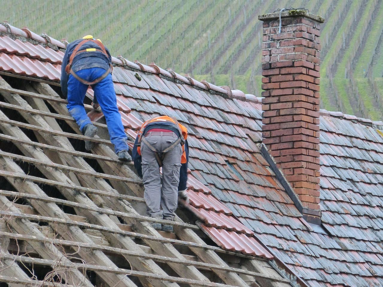 Roofers stripping an old slate roof back to the battens beside a brick chimney